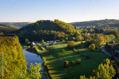 Sunrise in Herbeumont village with castle of Herbeumont on top of hill and campsite along riverside river Semois. Houses on countryside hills. Luxembourg province, Ardennes region, Wallonia, Belgium.