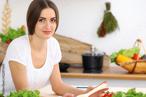 Beautiful Hispanic woman cooking while using tablet computer in kitchen. Housewife found new recipe for dinner or breakfast