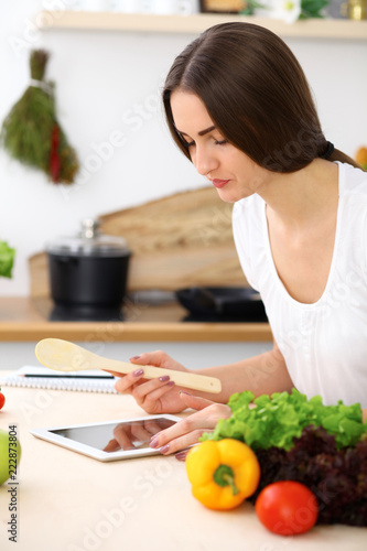 Beautiful Hispanic woman cooking while using tablet computer in kitchen. Housewife found new recipe for dinner or breakfast
