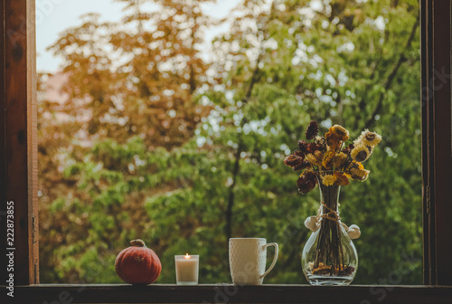 Cozy autumn still life: cup of hot coffee with autumn bouquet of flowers on vintage windowsill with cones and rain outside. Autumn. 