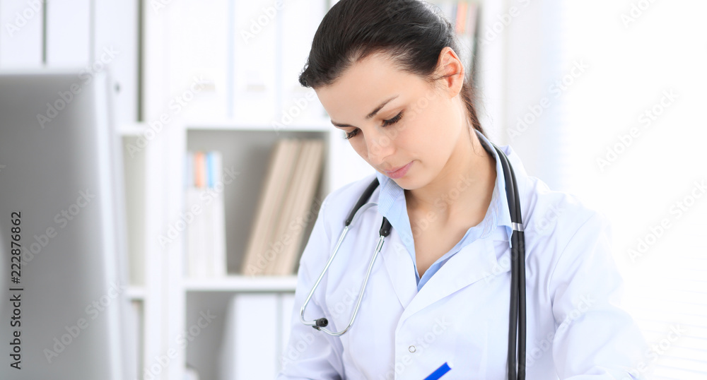 Young brunette female doctor at working place in hospital. Health care, insurance and help concept Young brunette female doctor at working place in hospital. Health care, insurance and help concept