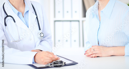 Unknown female doctor and patient discussing something while sitting at the table at hospital. Medicine and healthcare concepts