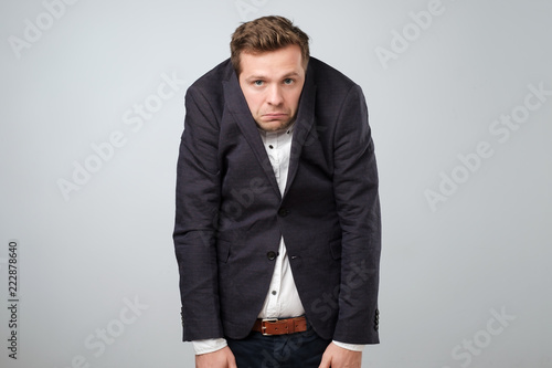 Caucasian young man in too big suit. He is offended and looking stressed. photo