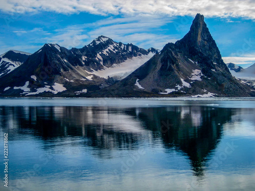 Dramatic mountains reflect in the calm, icy waters of Svalbard in the Norwegian high arctic