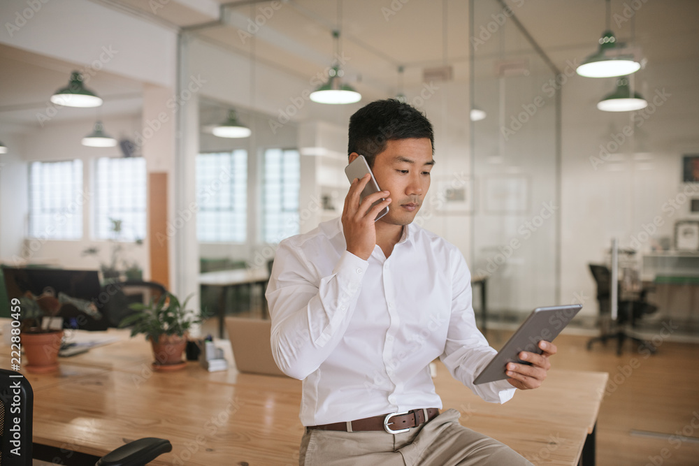© mavoimages - Asian businessman talking on his cellphone and using a tablet © mavoimages - Asian businessman talking on his cellphone and using a tablet