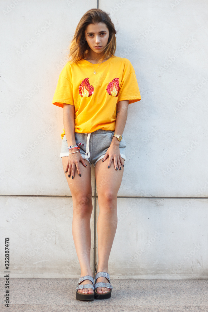 Fototapeta premium Portrait of a young woman posing on the street wearing a yellow shirt while the sun is shining. 