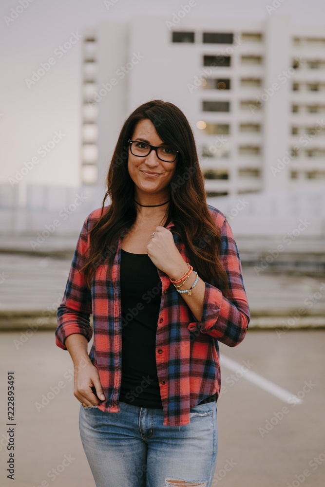 Cute Dark Haired Female Model Posing in Ripped Jeans and Plaid Shirt on Top Floor of Parking Garage