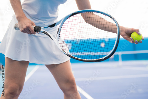 Mid-section closeup of unrecognizable young woman holding racket while playing tennis in indoor court, copy space