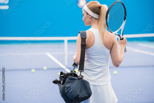 Back view portrait of beautiful blonde woman entering tennis court for practice, copy space