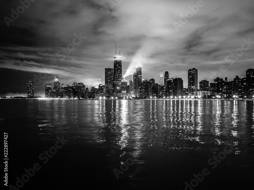 Beautiful Chicago night skyline photo with dramatic clouds above and building lights reflecting on the water of Lake Michigan.