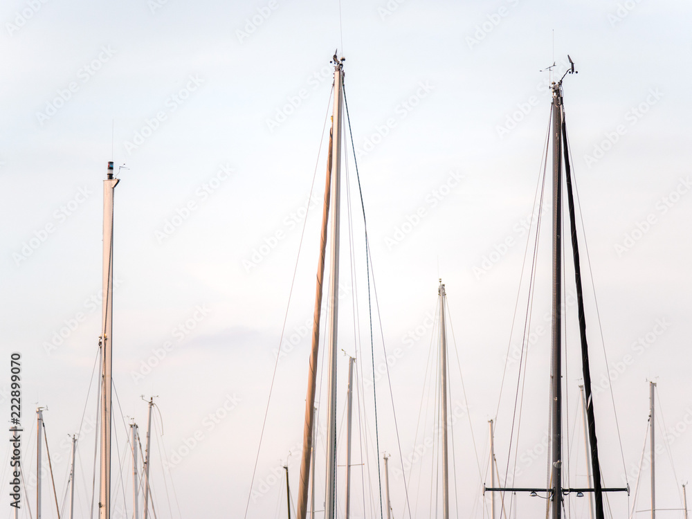 Closeup photograph of the top boat masts, weather vanes, and ropes of sailboats sitting in a harbor in Chicago with blue and cloudy sky above.