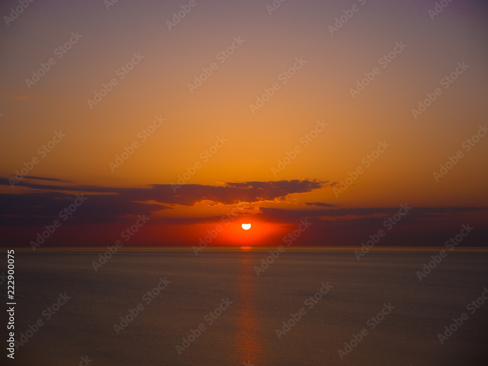 Beautiful sunrise photograph with vibrant orange and yellow colors over the dark waters of Lake Michigan in Chicago with layers of clouds in the sky above.