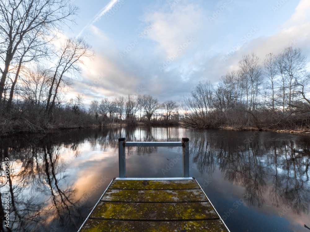 Obraz premium Beautiful landscape photograph of a weathered wood and steel pier sticking out into a pond in Wisconsin at sunset with the water reflecting the colorful clouds and trees making a fantastic background.