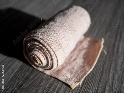 Close up photograph of a cream colored rolled up cloth compression bandage wrap for sports or other medical injuries or wounds laying on the floor with dark background and harsh shadows and lighting.