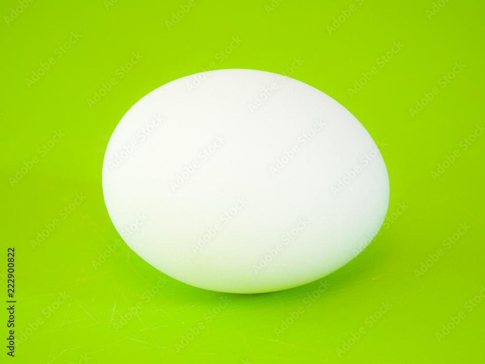 Close-up photograph of a real large white chicken egg on vibrant green solid color cutting board background making a beautiful eye catching background for the easter holiday. Close-up photograph of a real large white chicken egg on vibrant green solid color cutting board background making a beautiful eye catching background for the easter holiday.