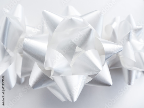 Close-up photograph of three manufactured shiny and pointy white ribbon bows centered and isolated on a white background making a perfect holiday or celebration background. photo