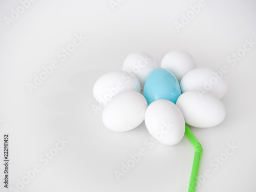Photograph of a cute flower shape created from the arrangement of white chicken eggs as petals and a blue plastic Easter egg and green flexible straw making a great holiday background image or craft.