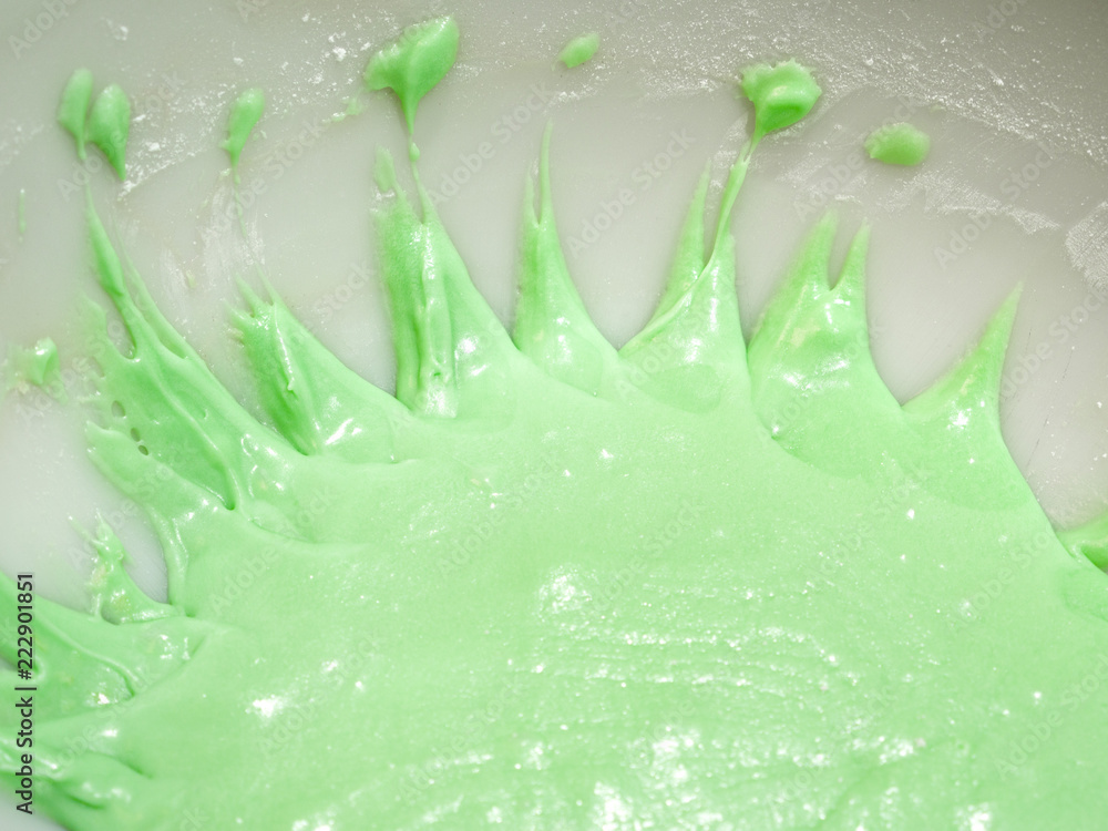 Obraz premium Close up view of pastel or mint green colored frosting with pointed splatter shaped edges in a white ceramic mixing bowl sitting on top of a kitchen counter.
