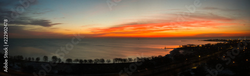 Beautiful wide panorama landscape photograph of a vivid red orange and yellow sunrise in Chicago over the water of Lake Michigan