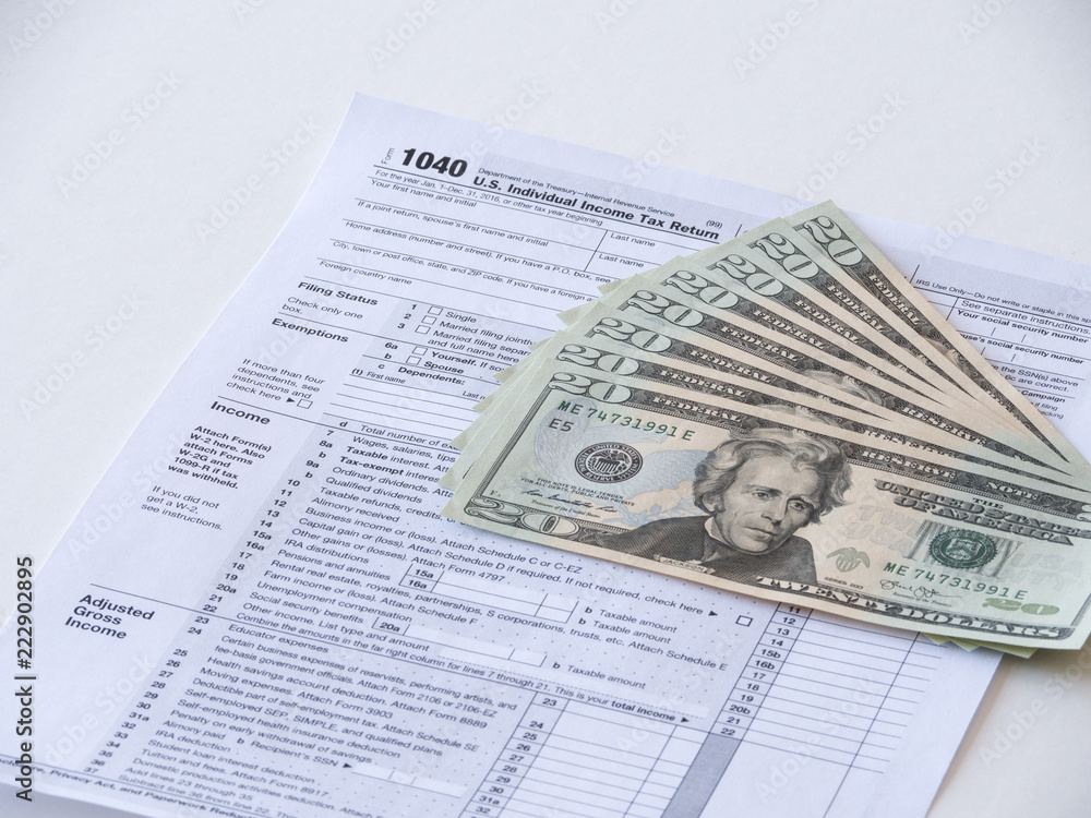 Obraz premium Close up photograph of 1040 individual earnings federal government department of treasury tax return with twenty dollar bills fanned out on top representative of tax deduction savings or fees.