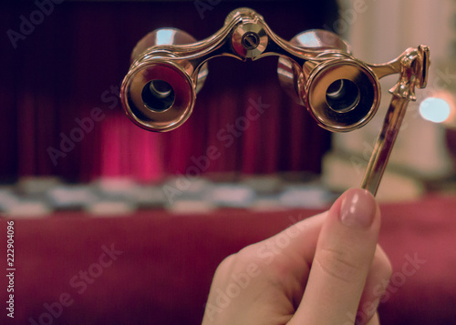 Obraz na plátně Woman hand holds opera glasses in theater against stage and drop-curtain