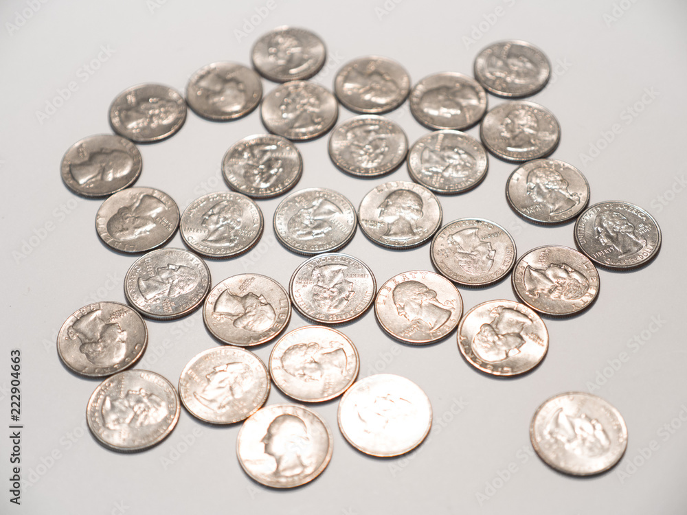 Close up photograph of a pile of quarters randomly laying on a white table top background. Close up photograph of a pile of quarters randomly laying on a white table top background.