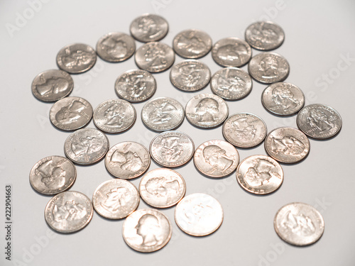 Close up photograph of a pile of quarters randomly laying on a white table top background.