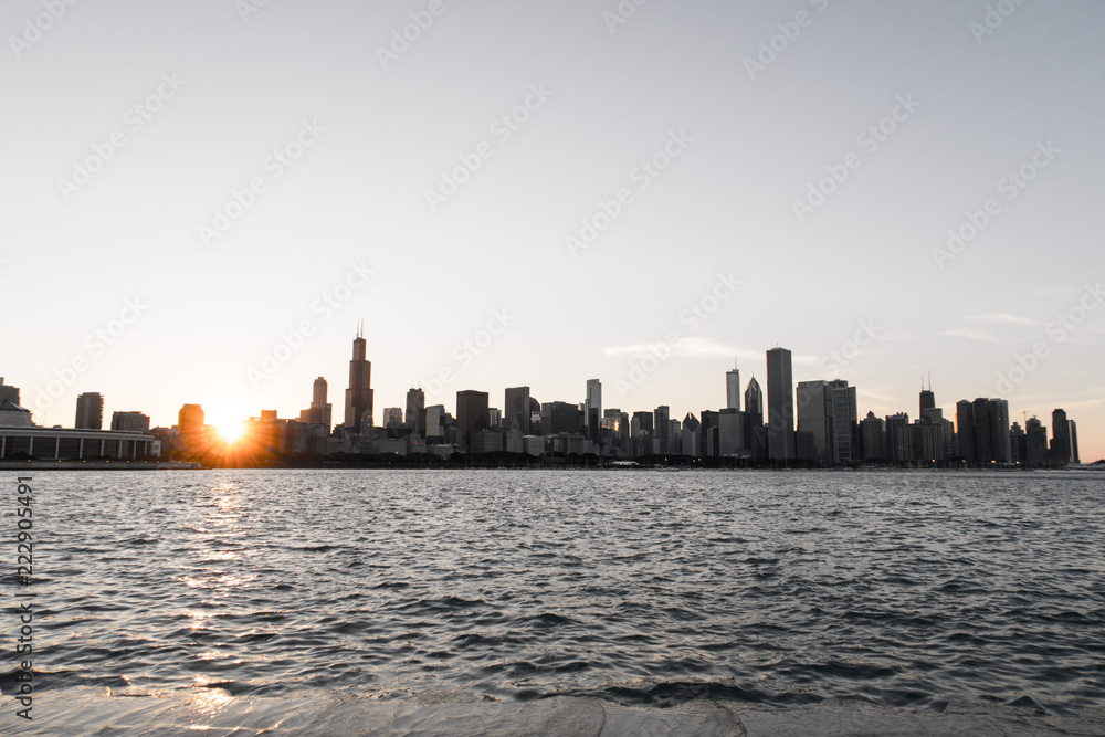 Chicago skyline picture during beautiful sunset with building silhouettes and rippling waves of Lake Michigan water in the foreground