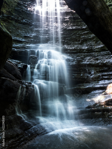 Beautiful photograph of a cascading waterfall in the Upper Dells in Mattiessen State Park in Illinois looking up at the falls from the riverbed below framed between limestone cliff and log above photo