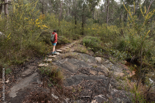 A female, baby boomer, hiker using steps up a rock on a hiking trail in Blackdown Tableland National Park, Queensland, Australia.