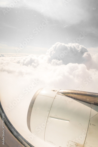 View looking down at jet engine and wing through window to agricultural land below  with white fluffy clouds above as the airplane travels across the sky