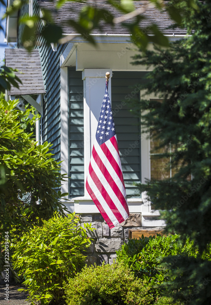 An American flag hanging in the front of a home in a neighborhood. Vertical photo and selective focus on the flag