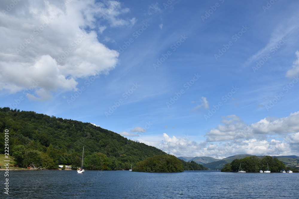 Blue sky and white clouds, the boat floats in the lake water, surrounded by green mountains
