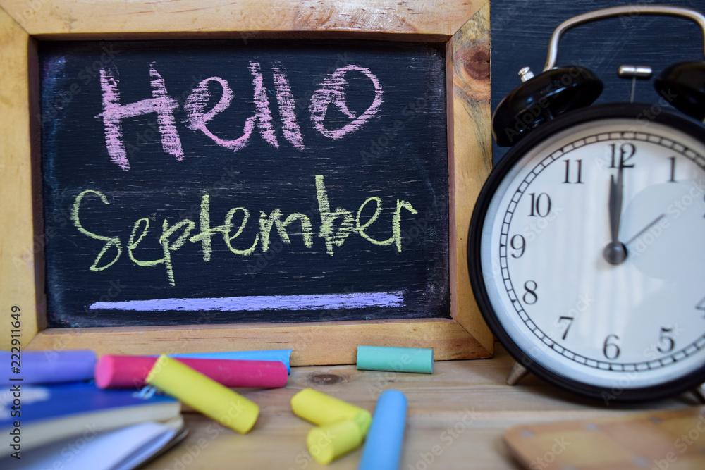 Hello september. Back to school concept. Alarm clock on wooden with blackboard on background Hello september. Back to school concept. Alarm clock on wooden with blackboard on background