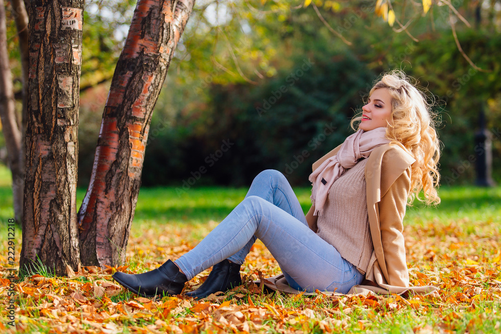 Young beautiful woman sitting on the ground coverd with fallen autumn leaves