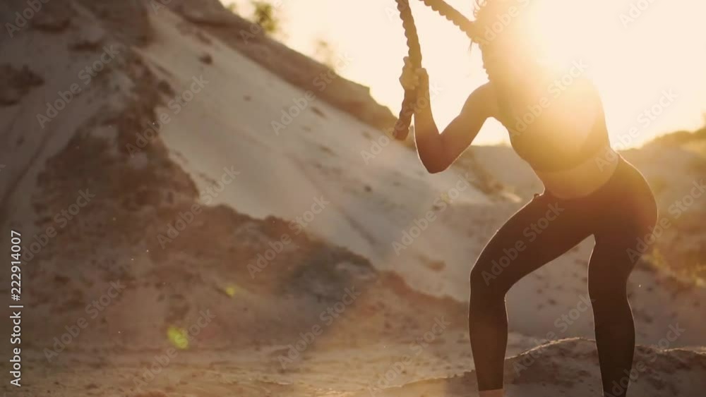 Close-up of a girl with a rope conducts outdoor training on the sandy ground near the beach. Rope in the hands of women at sunset