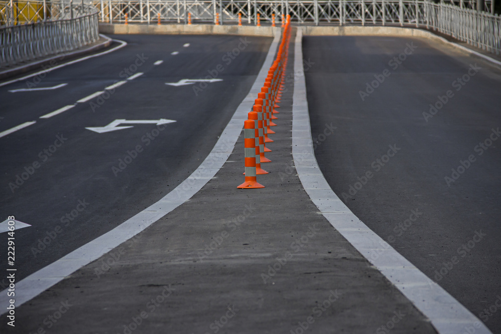 A line of safety traffic cones in the middle of a road with white lines and sign arrows