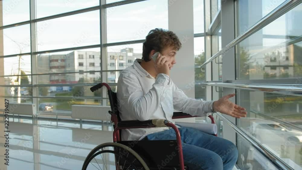 disabled businessman on a wheelchair at a window uses smartphone