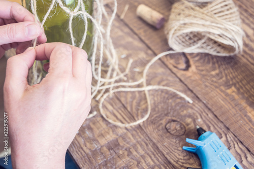 Woman decorating a bottle from wine with an ecological twine. Rustic style, handmade craft. Gift for christmas and other celebrations. Crafting process. Selective focus
