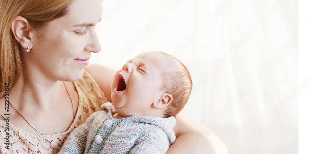Pretty woman holding yawning newborn baby in her arms. Close up image with copy space. Motherhood concept. Happy family concept. Copyspace Pretty woman holding yawning newborn baby in her arms. Close up image with copy space. Motherhood concept. Happy family concept. Copyspace
