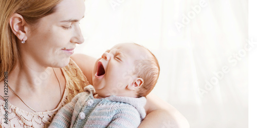 Pretty woman holding  yawning newborn baby in her arms. Close up image with  copy space. Motherhood concept. Happy family concept. Copyspace