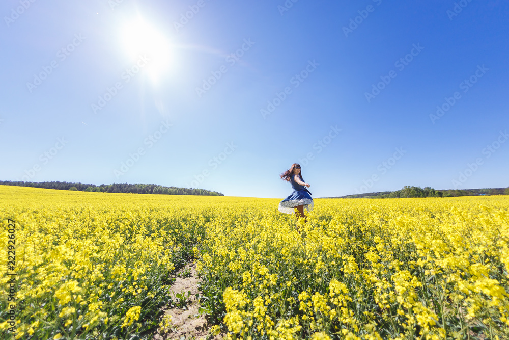 young happy beautiful  girl in a blue dress on blooming rapeseed field in summer. Follow me concept