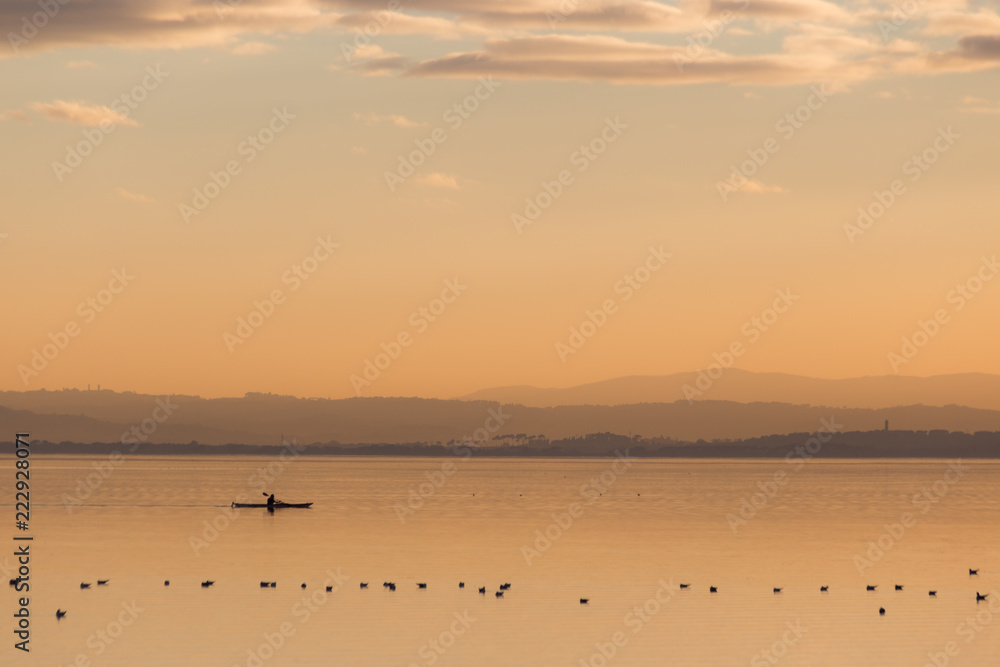 Beautiful view of a lake at sunset, with orange tones, birds on water and a man on a canoe