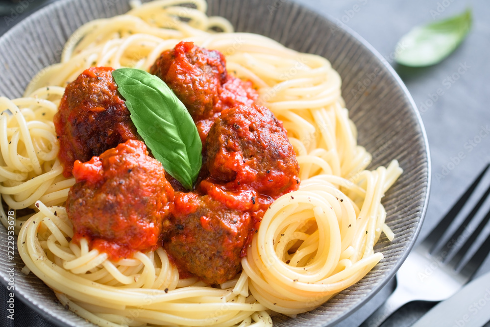 Beef meatballs in tomato sauce with Italian spaghetti and fresh basil leaf on a dinner table. Simply homemade recipe, close up. Beef meatballs in tomato sauce with Italian spaghetti and fresh basil leaf on a dinner table. Simply homemade recipe, close up.