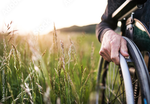 A close-up of man's hand on a wheelchair in nature at sunset. Copy space. photo
