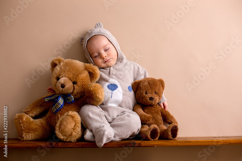 Sweet baby boy in bear overall, sleeping on a shelf with teddy bears