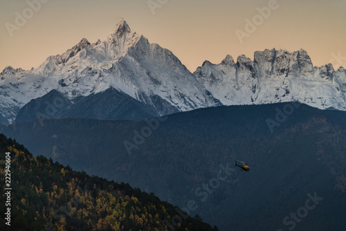 Meili snow mountain range with Mianzimu peak and tourist helicopter during sunrise in Deqing, Yunan province, China photo