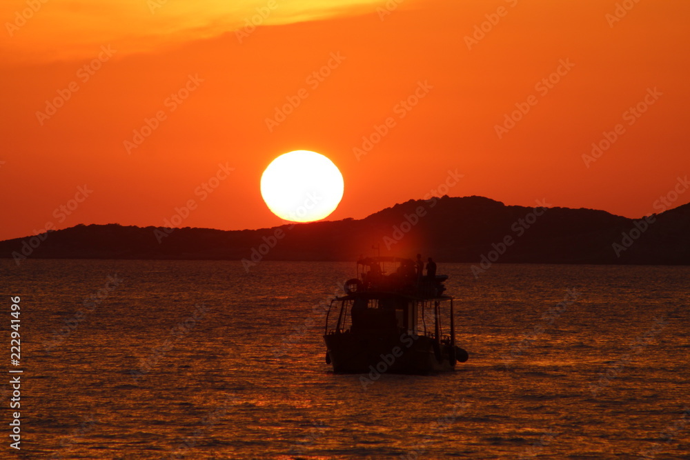 Sunset with orange sky, big sun going down and boat silhouette