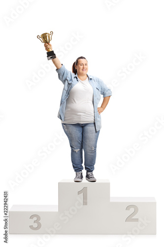 Overweight woman holding a gold trophy cup and standing on a winner's pedestal photo