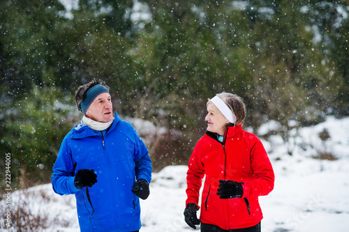 A front view of senior couple jogging in snowy winter nature.